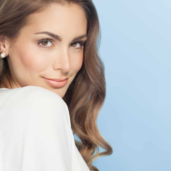Young beautiful woman with long hair posing and smiling over blue background. Fashion and beauty concept in studio.